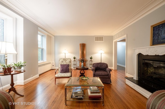 living room featuring visible vents, baseboard heating, wood finished floors, and ornamental molding