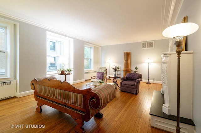 living room with light wood finished floors, visible vents, radiator heating unit, ornamental molding, and baseboards