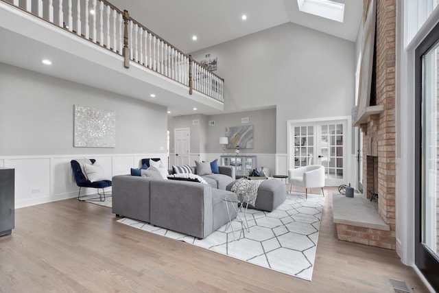 living area with high vaulted ceiling, a skylight, wood finished floors, visible vents, and a brick fireplace