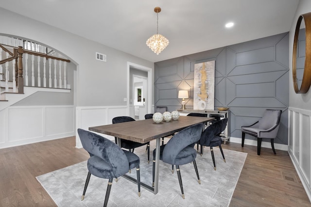 dining space with stairway, visible vents, a chandelier, and wood finished floors