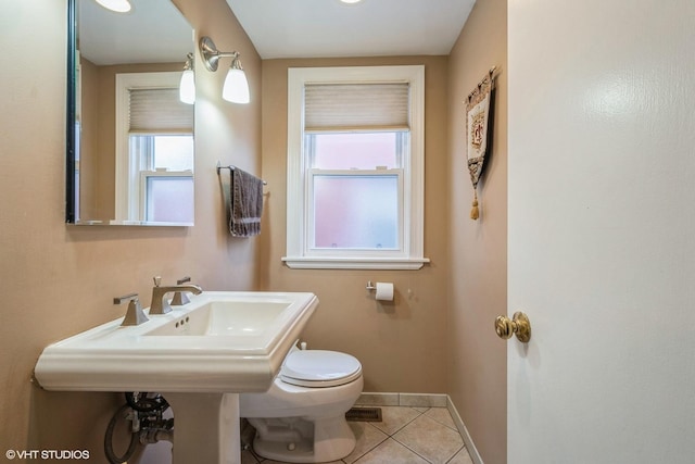 half bathroom featuring tile patterned flooring, baseboards, plenty of natural light, and toilet