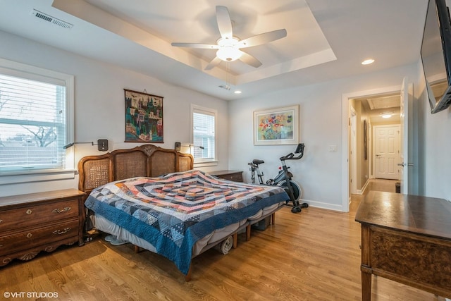 bedroom featuring a tray ceiling, visible vents, light wood-style floors, ceiling fan, and baseboards