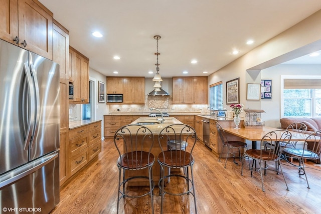 kitchen with stainless steel appliances, a sink, a kitchen breakfast bar, light wood-type flooring, and decorative backsplash