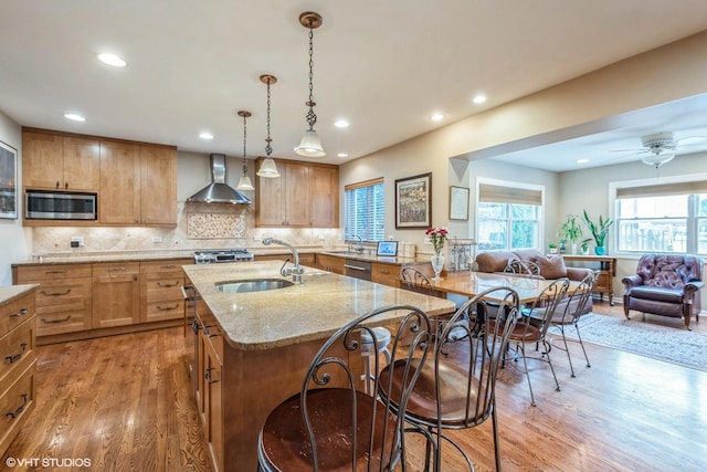 kitchen featuring light stone counters, appliances with stainless steel finishes, open floor plan, a sink, and wall chimney range hood