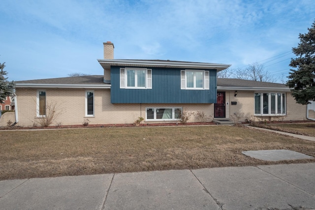 tri-level home with a front lawn, a chimney, and brick siding