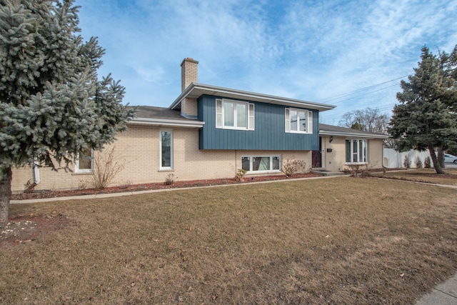 split level home featuring a front lawn, a chimney, and brick siding