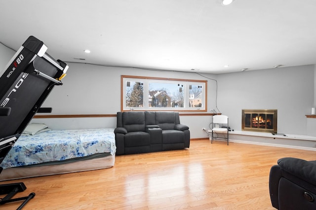 bedroom featuring wood finished floors, a glass covered fireplace, visible vents, and recessed lighting