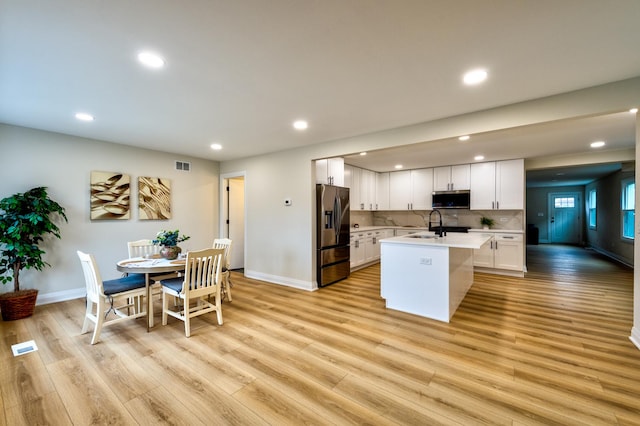 kitchen with black fridge with ice dispenser, white cabinetry, light countertops, stainless steel microwave, and an island with sink