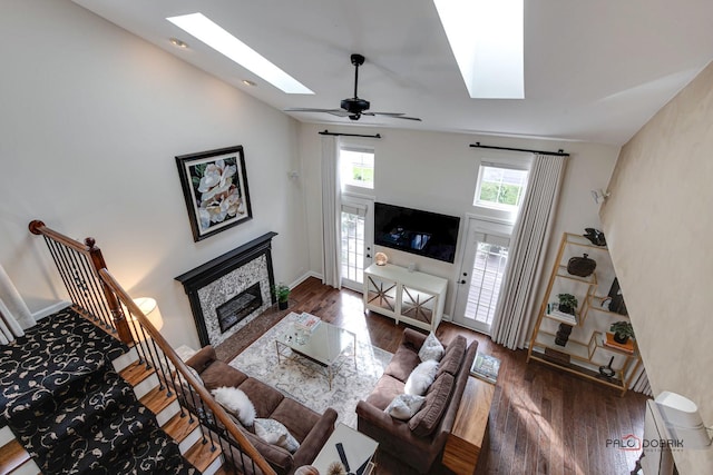 living room featuring a skylight, stairway, a glass covered fireplace, wood finished floors, and baseboards