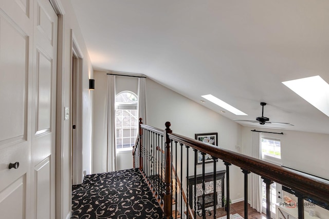 hallway with lofted ceiling with skylight and an upstairs landing