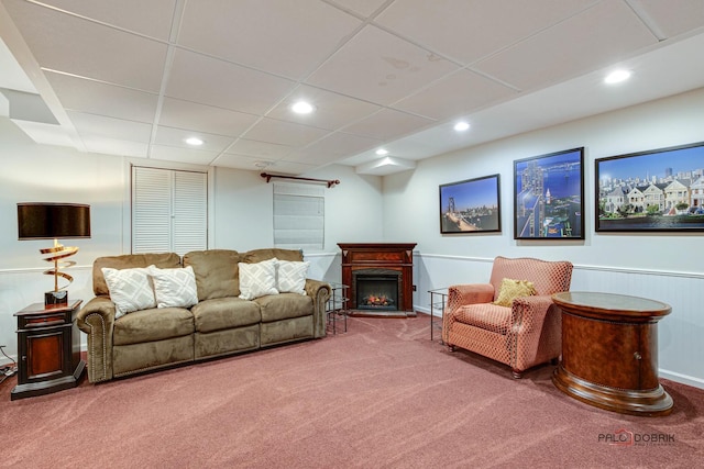 carpeted living room with a warm lit fireplace, a wainscoted wall, a paneled ceiling, and recessed lighting