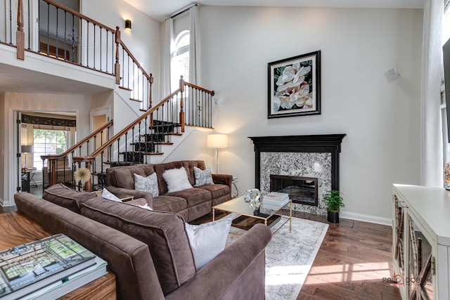 living room featuring dark wood-style floors, a fireplace, a high ceiling, baseboards, and stairs