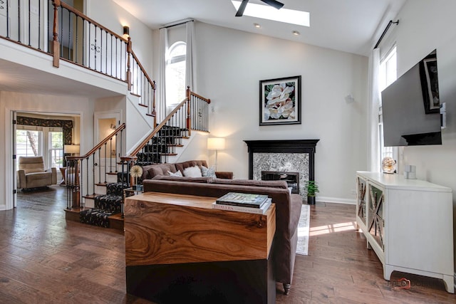 bedroom featuring high vaulted ceiling, hardwood / wood-style flooring, a skylight, baseboards, and a glass covered fireplace