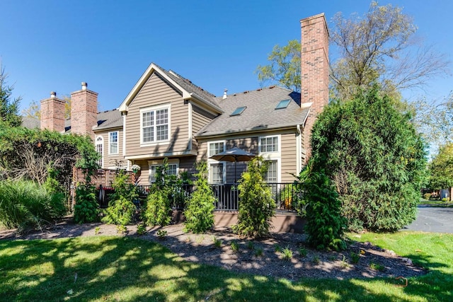 back of property with a chimney, a lawn, and a wooden deck