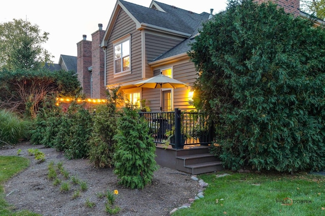 view of front of home with a deck, roof with shingles, and a chimney