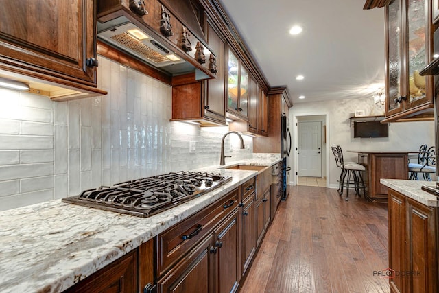 kitchen featuring dark wood-style floors, light stone counters, premium range hood, gas cooktop, and a sink