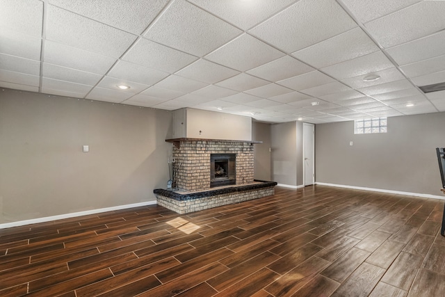 unfurnished living room with a paneled ceiling, a brick fireplace, baseboards, and dark wood-type flooring