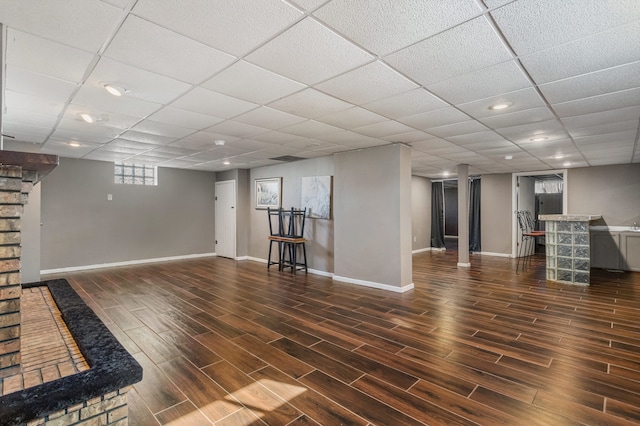 below grade area with a paneled ceiling, dark wood finished floors, a dry bar, and baseboards