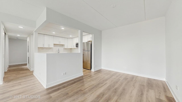 kitchen with baseboards, white cabinets, freestanding refrigerator, light countertops, and light wood-style floors