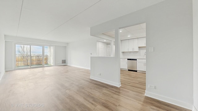 unfurnished living room featuring visible vents, a sink, light wood-style flooring, and baseboards