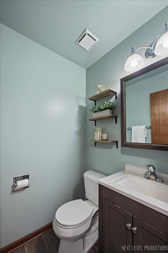 bathroom featuring toilet, wood finished floors, vanity, visible vents, and baseboards