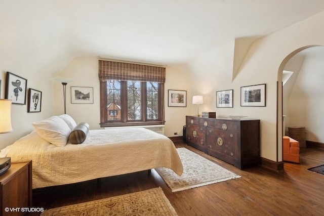 bedroom with lofted ceiling, arched walkways, baseboards, and wood finished floors