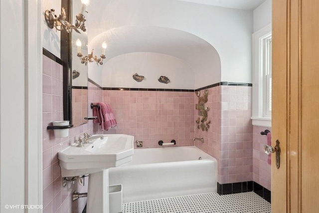 full bath with a tub to relax in, tile patterned floors, tile walls, and an inviting chandelier