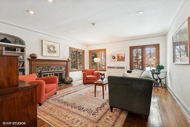 sitting room with wood-type flooring, built in features, baseboards, and a high end fireplace