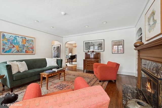 living room with baseboards, arched walkways, ornamental molding, wood finished floors, and a fireplace