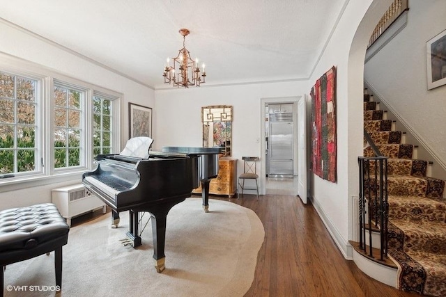 sitting room featuring radiator heating unit, stairway, wood finished floors, an inviting chandelier, and crown molding