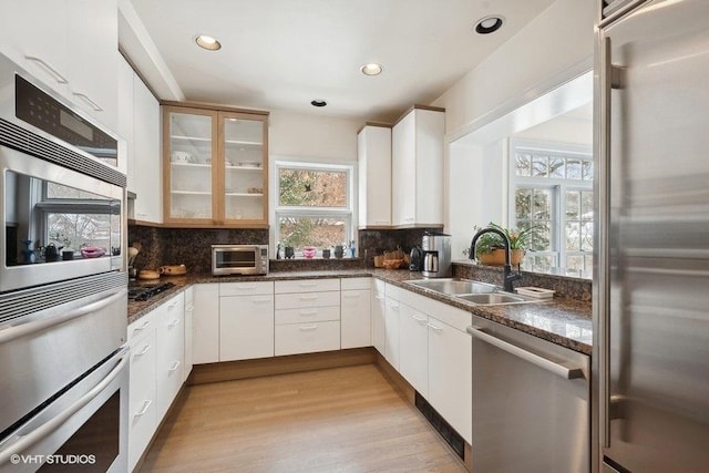 kitchen featuring appliances with stainless steel finishes, glass insert cabinets, a sink, and backsplash