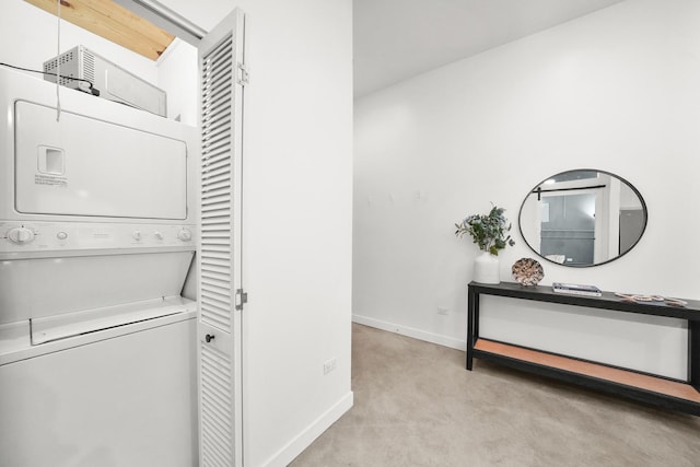 clothes washing area featuring laundry area, stacked washing maching and dryer, and baseboards