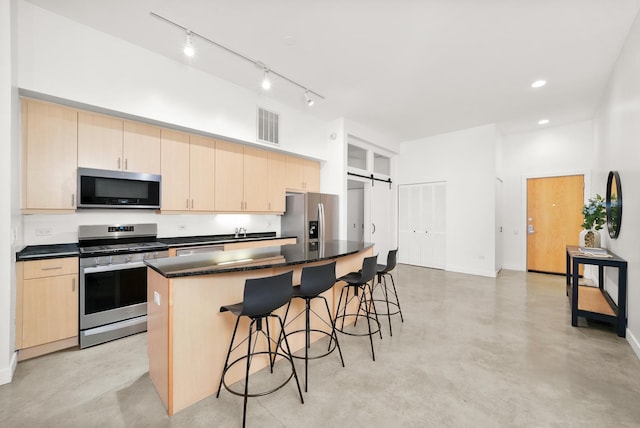 kitchen featuring a barn door, finished concrete flooring, appliances with stainless steel finishes, a center island, and dark countertops