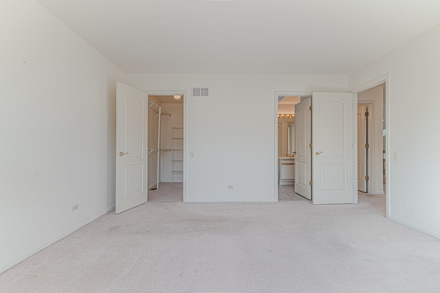 unfurnished bedroom featuring a spacious closet, visible vents, baseboards, carpet flooring, and ensuite bath