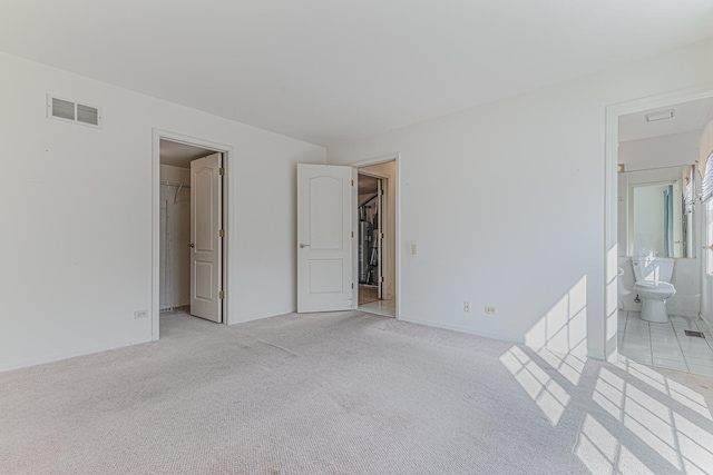 unfurnished bedroom featuring visible vents, ensuite bath, a closet, light colored carpet, and a spacious closet