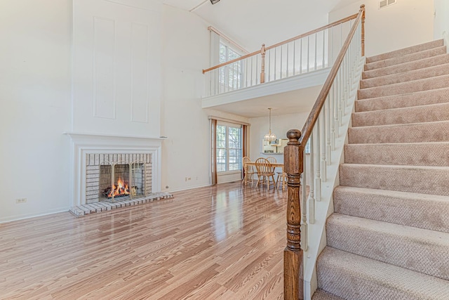 staircase with visible vents, a brick fireplace, baseboards, wood finished floors, and high vaulted ceiling