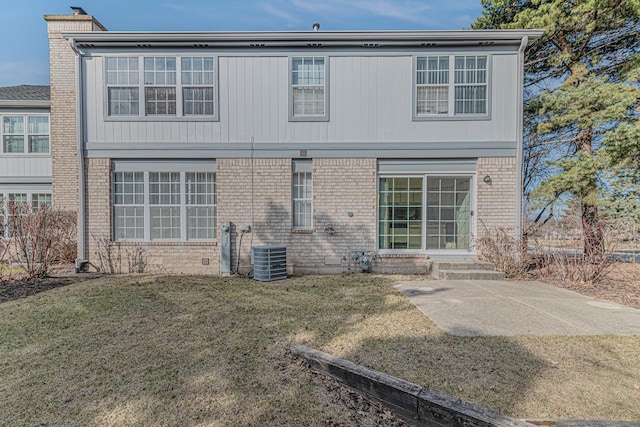 back of property featuring brick siding, entry steps, cooling unit, a chimney, and a yard