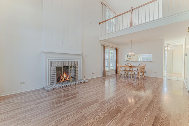 living room with wood finished floors, a towering ceiling, baseboards, a brick fireplace, and ceiling fan