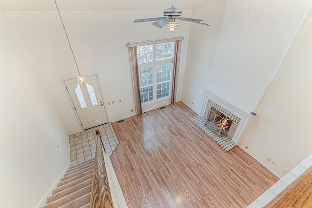 foyer entrance with a brick fireplace, light wood-style floors, a high ceiling, and ceiling fan