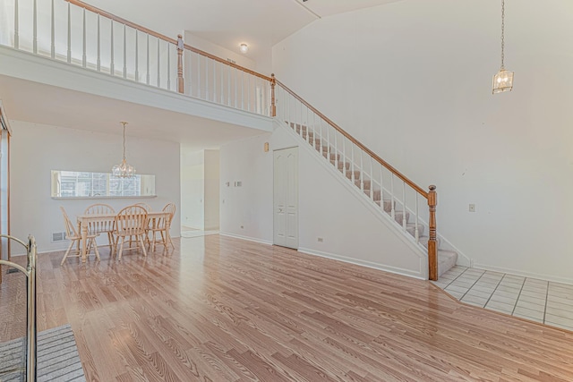 unfurnished living room featuring a chandelier, high vaulted ceiling, wood finished floors, and stairway