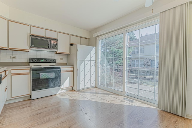 kitchen with range with electric cooktop, black microwave, decorative backsplash, light wood-style flooring, and freestanding refrigerator