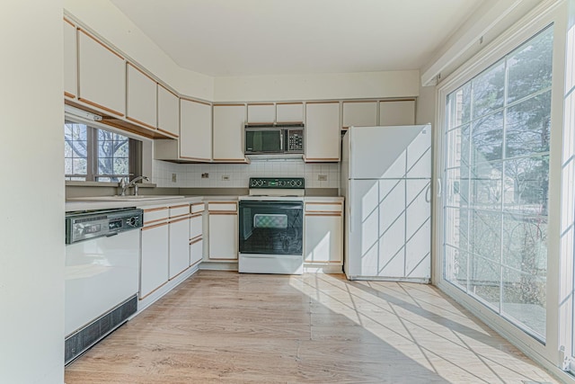 kitchen with light wood finished floors, a sink, backsplash, white appliances, and light countertops