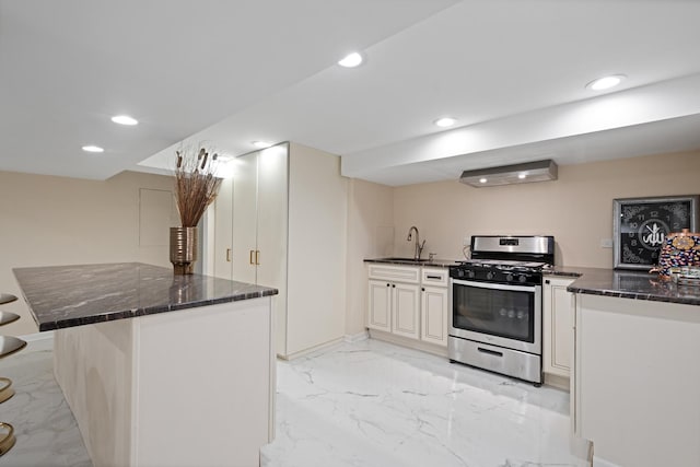 kitchen featuring stainless steel gas stove, dark stone counters, marble finish floor, a sink, and recessed lighting