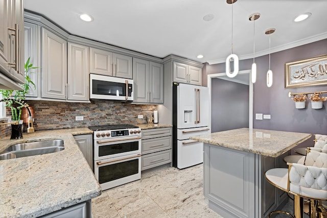 kitchen featuring premium appliances, tasteful backsplash, gray cabinetry, a sink, and a kitchen breakfast bar