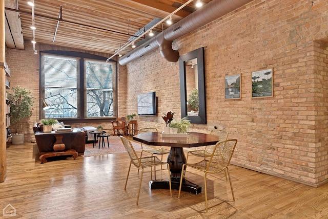 dining room with brick wall, rail lighting, a high ceiling, and wood finished floors