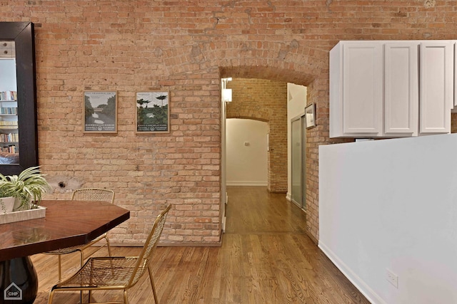 hallway with arched walkways, brick wall, baseboards, and light wood-style floors