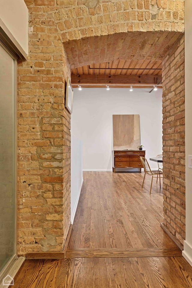 hall with brick wall, beamed ceiling, wood finished floors, and baseboards