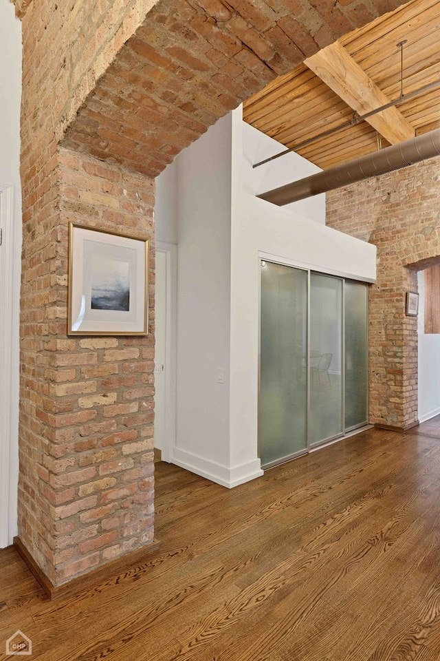 unfurnished room featuring brick ceiling, baseboards, brick wall, and wood finished floors