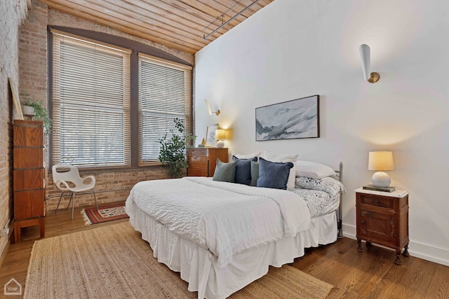 bedroom featuring baseboards, lofted ceiling, wood ceiling, brick wall, and wood finished floors