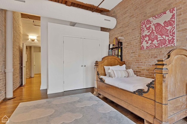 bedroom featuring brick wall, a high ceiling, a closet, and wood finished floors